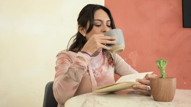 Mujer latina en una cafeter&iacute;a leyendo un libro y tomando un caf&eacute;.