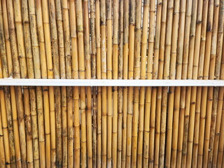 Fence made from bamboo secure with white colored wooden boards for durability and strength. Dried bamboo wall or fence. Fence made from natural materials. The fence is made of vertical bamboo trunks.
