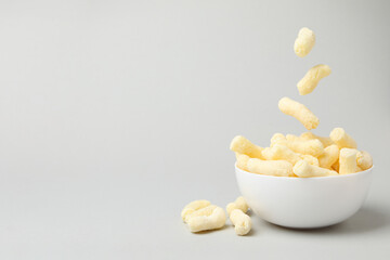 Sweet corn sticks falling in bowl on light gray background, space for text
