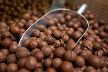 A pile of macadamia nuts on the supermarket counter. The scoop for the set of nuts lies on top of the nuts. Environmental products