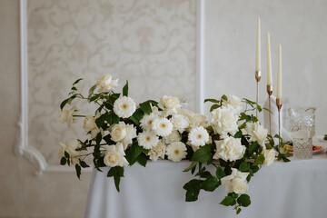 A table with a white tablecloth and a vase of white flowers. The flowers are arranged in a way that they look like they are cascading down the table. The table is set for a special occasion