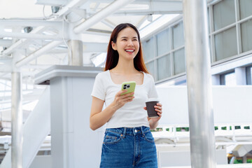 Woman holding smartphone with coffee cup while walking in the urban city.