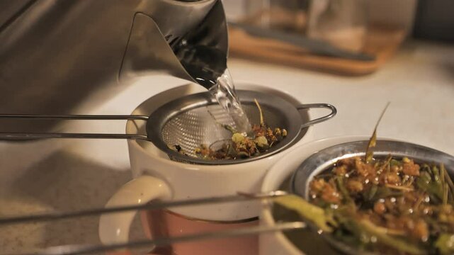 Hot water poured into a tea strainer over herbs - 4K.