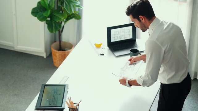 Architect engineer using laptop planning house design at office while sitting at meeting table with blueprint and equipment scatter around.Skilled civil engineer working at blueprint. Alimentation.