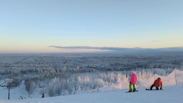 Snowboarder newbie falling down the piste of winter ski resort, white snowy landscape with people skiing in a distance. Outdoor activities and training in cold weather, forest trees covered with snow