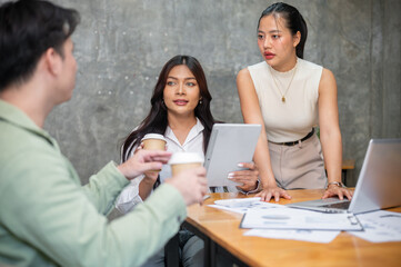 Two Asian businesswomen are focused on listening to their colleague's ideas in the meeting.