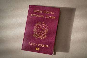 Italian passport lying on textured surface casting shadow