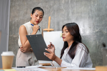 Two focused Asian businesswomen are reviewing documents together during the meeting.