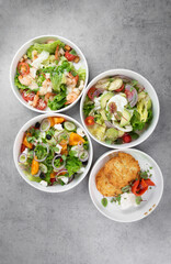 Three different vegetable salads and slavic draniki (potato pancakes) on gray marble background