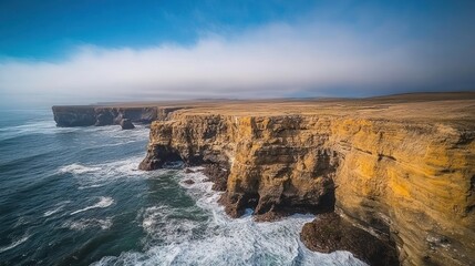 A dramatic view of a rocky coastline with crashing waves and a hazy sky.