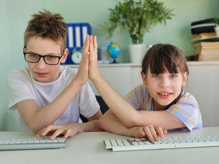 Two children engaged in a friendly competition while using computers