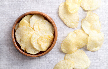 Salted potato chips in a wooden bowl on linen fabric. Fresh and ready to eat crisps, slim slices of deep fried potato, made from tubers of the root vegetable Solanum tuberosum. Close-up, from above.