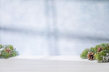 Christmas template featuring snowy fir tree branches on a table with shadows and sun glares softly falling on the wall