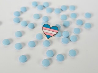 Transgender pride pin surrounded by blue tablets on a white surface, symbolizing LGBTQ