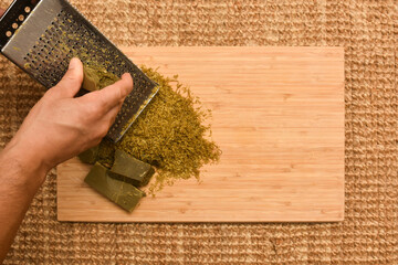 Close-up of a man's hand grating Marseille soap on a board to prepare homemade detergent