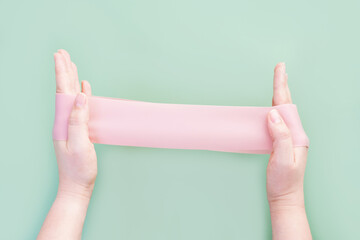 Hands stretching fitness elastic band on green background close-up.