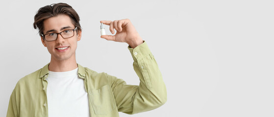 Young man in glasses with eye drops on light background. Glaucoma awareness month