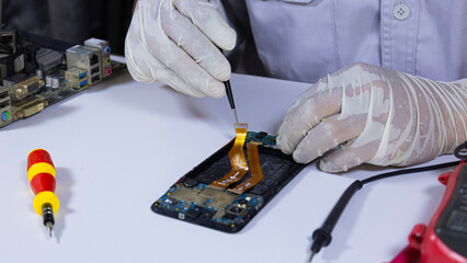 The asian technician uses pliers to clamp telephone cable to repair smartphone. Technician repairing inside of mobile phone. Concept of  hardware, electronic and computer Engineering, technology.