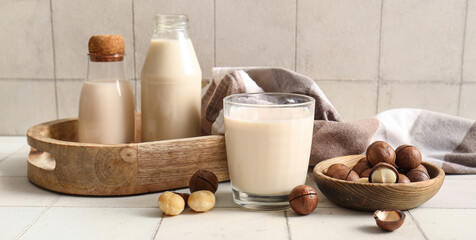 Glass and bottles of fresh macadamia milk on white tile background