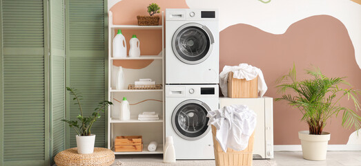 Washing machines, dryer, shelving unit and baskets with clothes in interior of laundry room