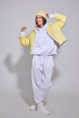 Fashion asian female model in white sport suit,  sneakers, yellow hat and down jacket.