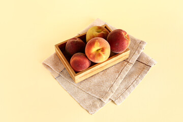 Wooden box with sweet peaches on yellow background