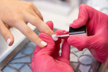 Skilled nail technician in pink gloves carefully paints gel polish on a womans nails in a cozy salon