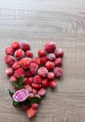 Frozen strawberries arranged in the shape of a heart on a wooden table decorated with green leaves. Romantic and inviting presentation.
