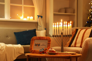 Greeting card for Hannukah with dreidels, doughnut and menorah on table in dark living room