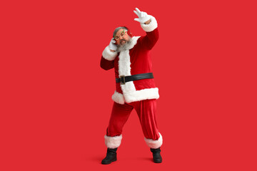 Funny Santa Claus in headphones listening to music and dancing on red background