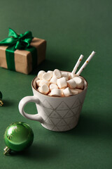 Cup of hot cocoa with marshmallows and Christmas gift box on green background