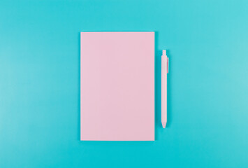 Top view of pink notebook, pink pen on blue background. School, office wallpaper. Flat lay, copy space.