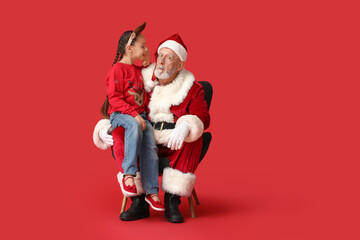 Cute little girl telling Santa Claus her wish on armchair against red background