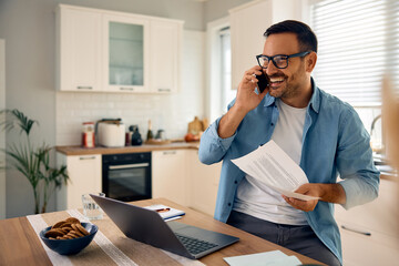 Happy man talking on cell phone while going through paperwork at home.