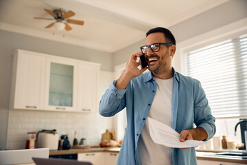 Happy businessman talking on cell phone while working on reports at home.