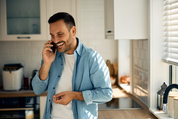 Happy man having phone call over cell phone in  kitchen.