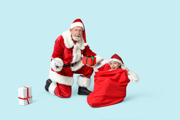 Santa Claus and cute little girl with gift boxes in bag on blue background