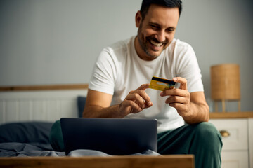 Happy man using credit card and laptop for online shopping.