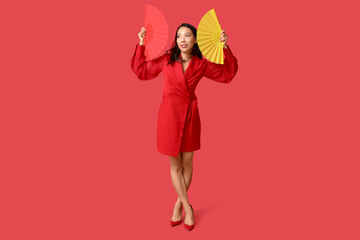 Beautiful young happy Asian woman with fans on red background. Chinese New Year celebration