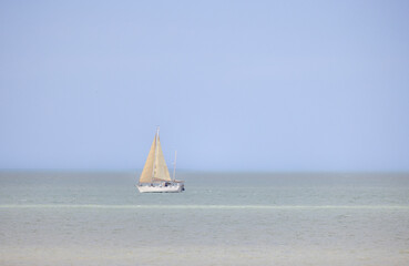 A beautifully tranquil view of a sailboat gliding effortlessly on calm waters beneath a vast blue...
