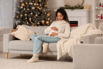Fototapeta premium Pregnant African-American woman resting at home on Christmas eve
