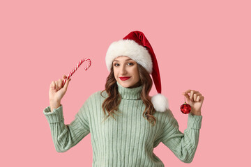 Fototapeta premium Young woman in Santa hat with Christmas ball and candy cane on pink background