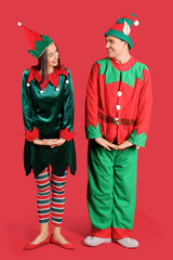 Happy couple in elf's costumes on red background