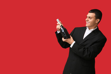 Young man with bottle of champagne celebrating Christmas on red background