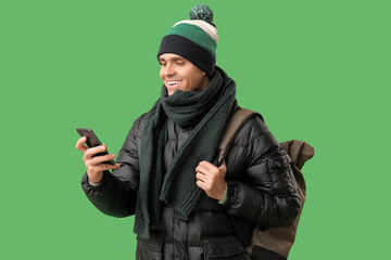Young man in stylish puffer jacket with mobile phone and bag on green background