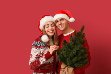 Happy young couple in Santa hats with Christmas tree on red background