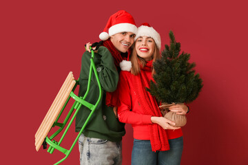 Beautiful young couple with Christmas tree and sled on red background