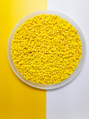 Yellow masterbatch granules in a cup on a yellow and white background, a color pigment carrier polymer in the plastics industry.