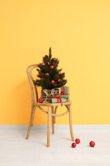 Wooden chair with Christmas tree in pot and gifts near orange wall