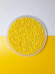 Yellow masterbatch granules in a cup on a yellow and white background, a color pigment carrier polymer in the plastics industry.